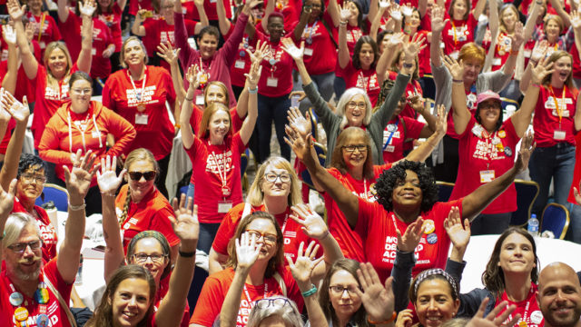 A large crowd of Moms Demand Action volunteers raise their arms in the air at the Gun Sense University conference