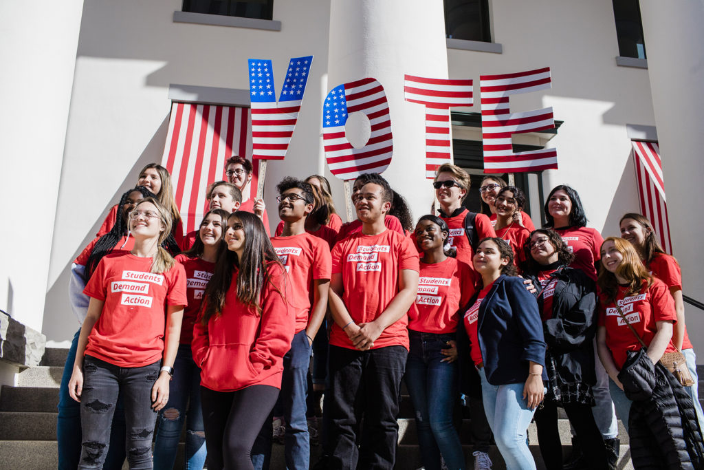 A group of about 20 Students Demand Action volunteers stand with a large VOTE sign