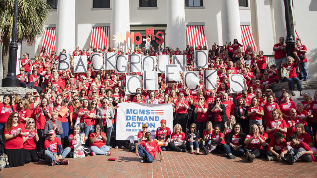 A large group of Moms Demand Action volunteers hold up signs spelling, 'Background Checks' at an Advocacy Day in Florida
