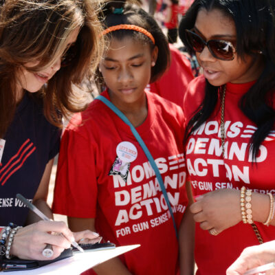 Three volunteers in Moms Demand Action and Gun Sense Voter shirts look at a clipboard together
