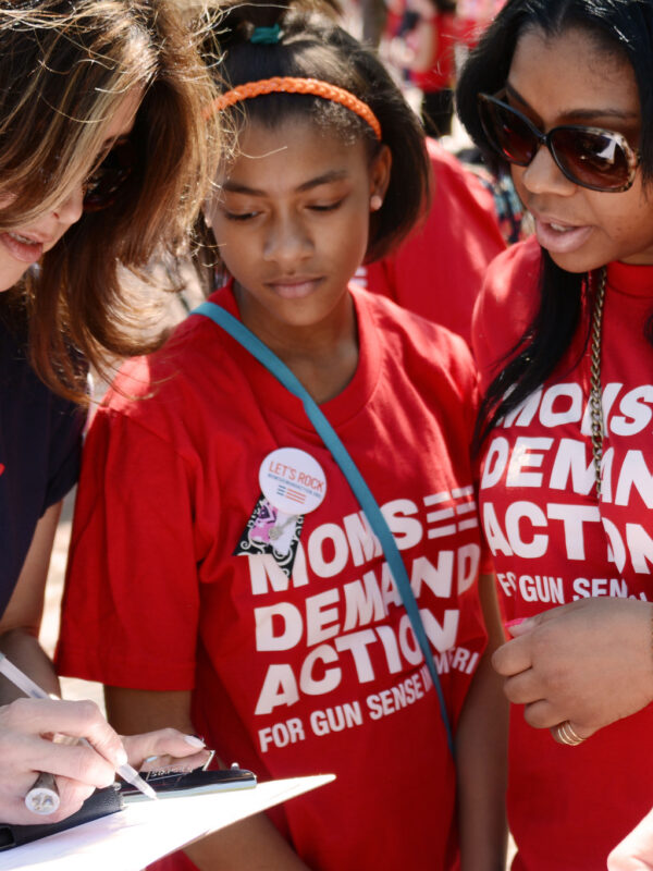 Three volunteers in Moms Demand Action and Gun Sense Voter shirts look at a clipboard together