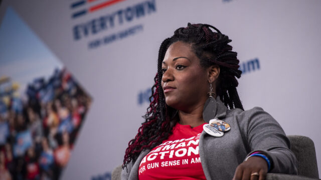 DeAndra Dycus a Moms Demand Action volunteer and survivor of gun violence sits in a chair on the stage at the Gun Sense Forum in 2019
