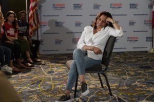 Kamala Harris sits with her legs crossed while smiling as she talks to a group of volunteers at the Gun Sense Forum in 2019. 