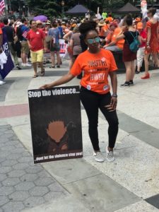 Nathalie Arzu stands at an event with a sign that says, 'stop the violence... don't let the violence stop you'