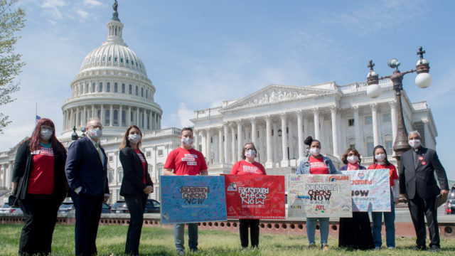 A group of nine volunteers, staff, and elected officials stand with Background Checks Now murals at the Capitol at the final stop of the Road Trip for Background Checks