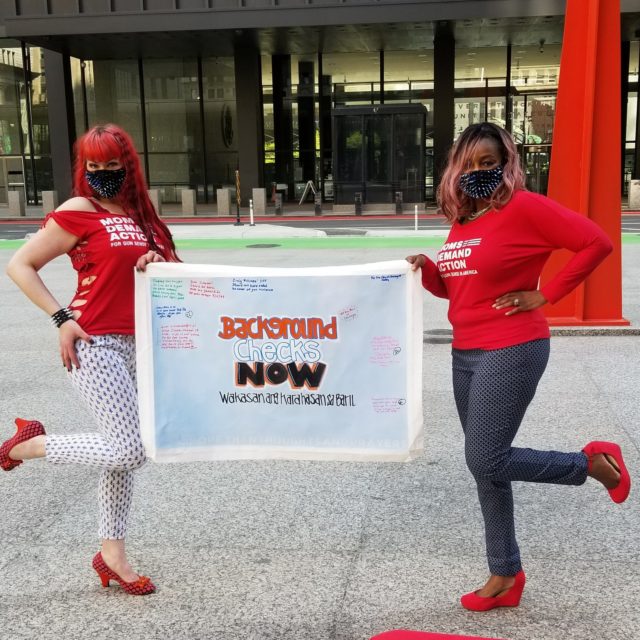 Two volunteers in Chicago hold up the Background Checks Now sign on the Road Trip for Background Checks