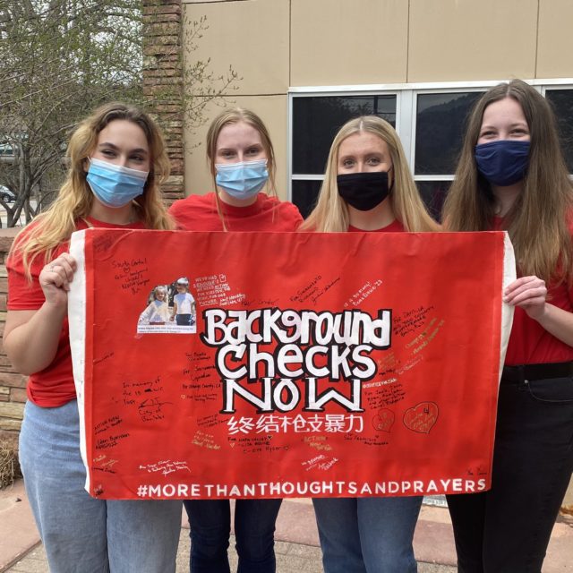 Four volunteers in Colorado hold up the Background Checks Now sign