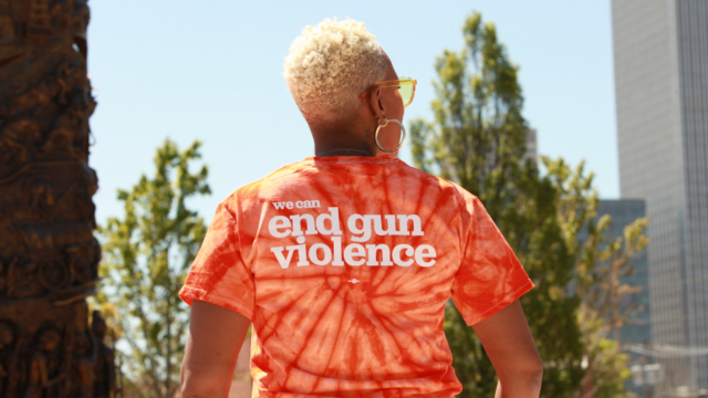 The back profile of a woman wearing a tie-dyed Wear Orange shirt that says
