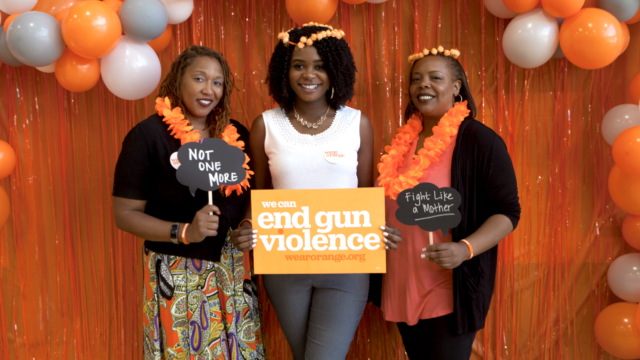 Three people dressed for Wear Orange festivities and holding signs pose for a photo