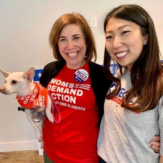 Norri Leder smiles while holding a dog and wearing a Moms Demand Action shirt with another volunteer