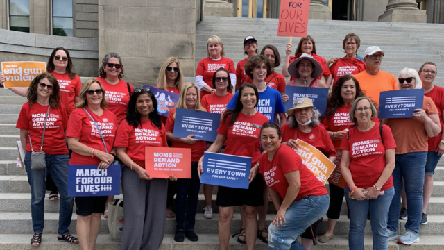 Idaho Moms Demand Action volunteers pose for a photo and hold signs, wearing their red Moms Demand Action t-shirts