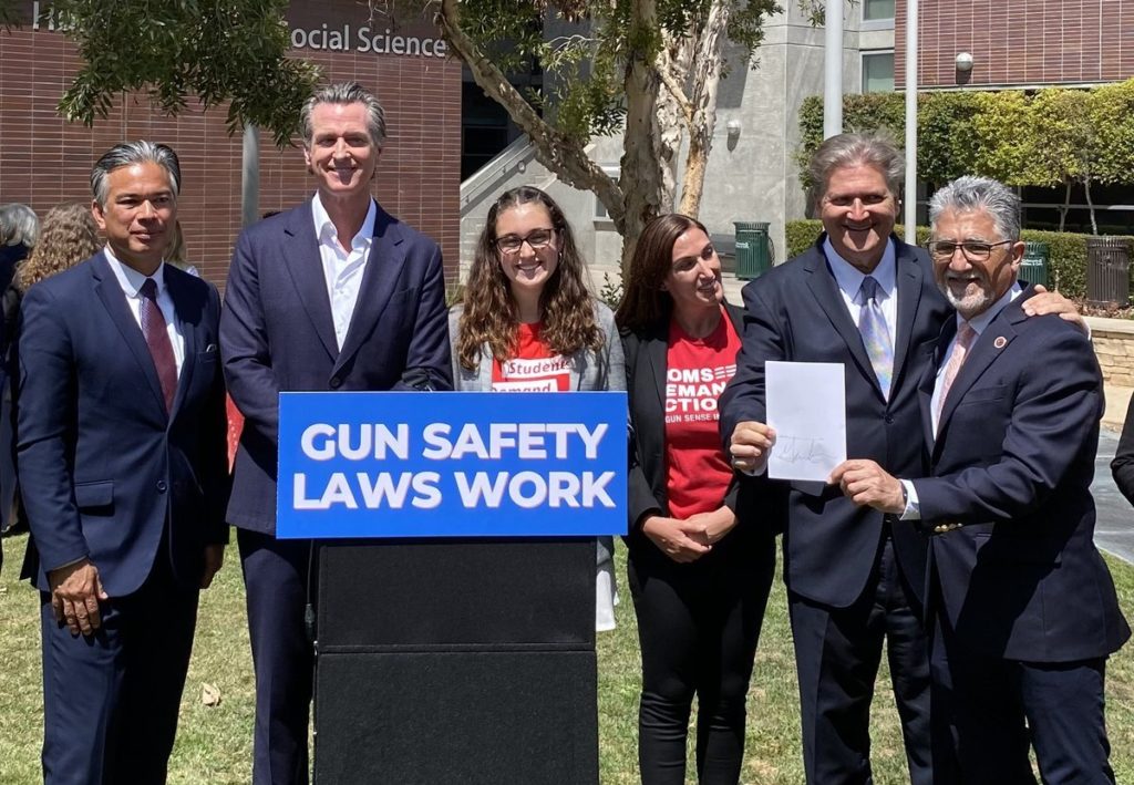 California Governor Gavin Newsom poses with a Students Demand Action volunteer, Moms Demand Action volunteer, and three other suited individuals