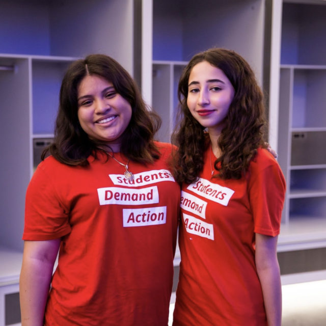 Ashley Castillo poses for a photo with another Students Demand Action volunteer. They are both wearing red Students Demand Action t-shirts.