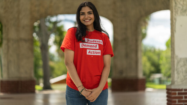 Neha Bengalore poses for a photo standing and wearing a red Students Demand Action t-shirt