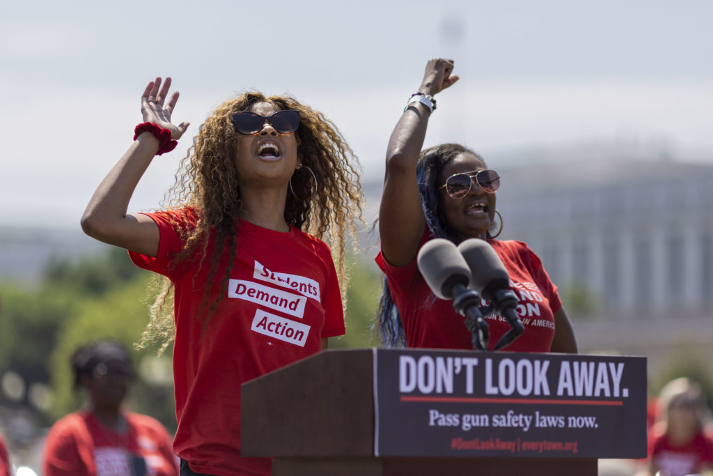 A Students Demand Action volunteer and a Moms Demand Action volunteer stand at a podium while looking up with raised arms