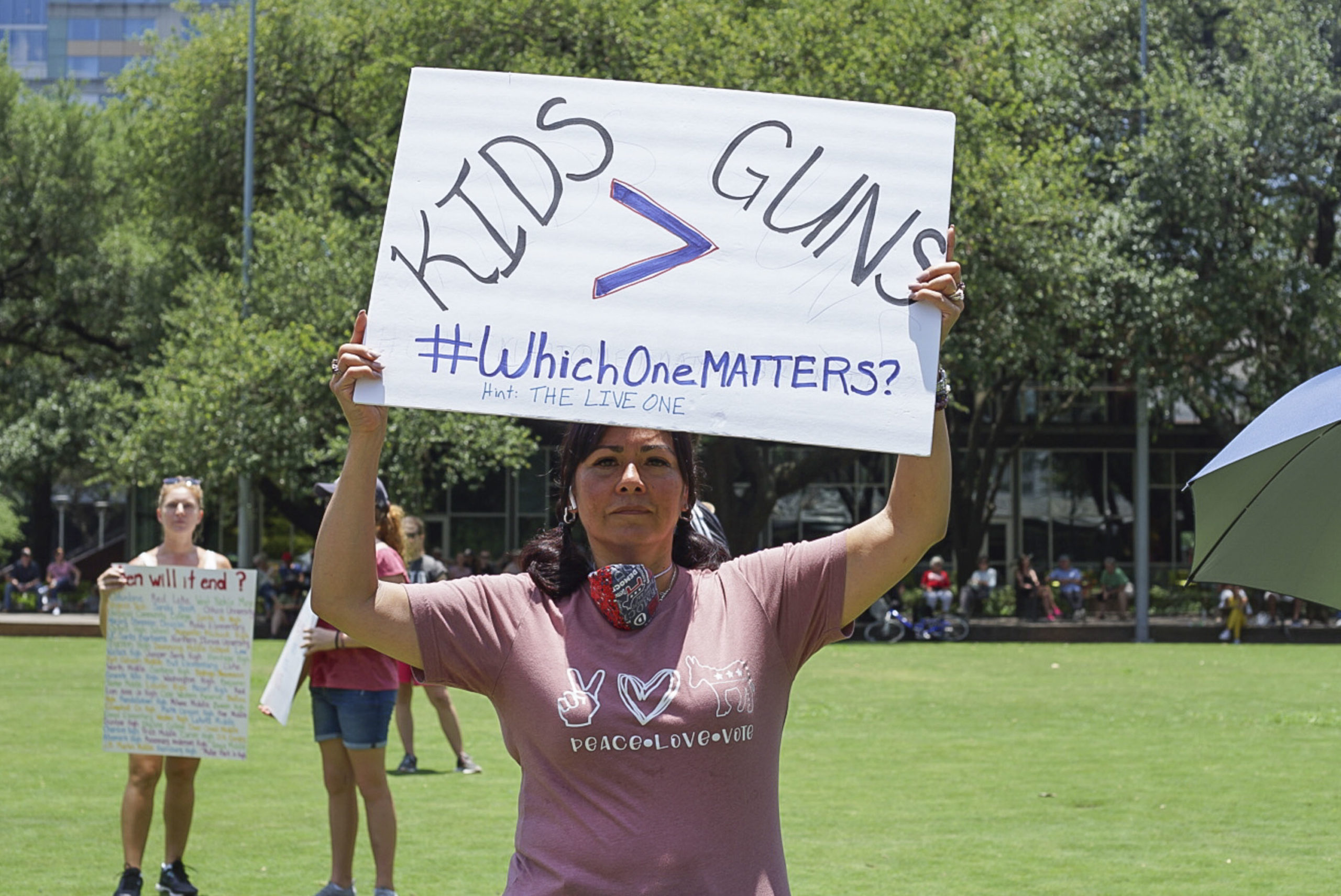 A woman holds up a sign that says "Kids > Guns. #WhichOneMATTERS?" outside the NRA Convention