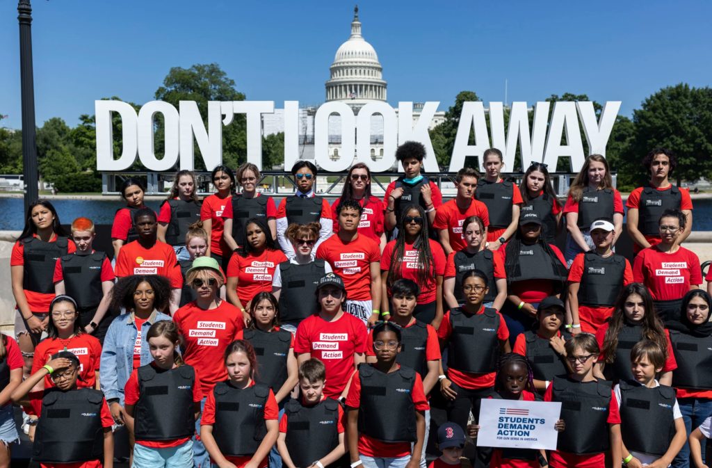 Students standing at the Capitol wearing red Students Demand Action t-shirts and black bulletproof vests