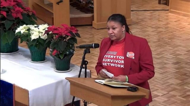 Donnitta Marie Sinclair wearing a red Everytown Survivor Network t-shirt and speaking at a podium