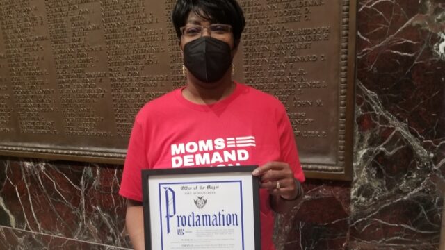 Jenevia Blanks holding a framed proclamation from the Office of the Mayor