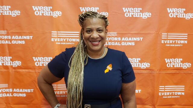 Mayor Shawyn Patterson-Howard wearing an orange ribbon in front of a Wear Orange backdrop