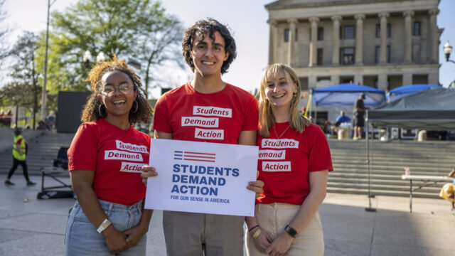 Students Demand Action volunteers wearing red Students Demand Action t-shirts and holding a Students Demand Action sign