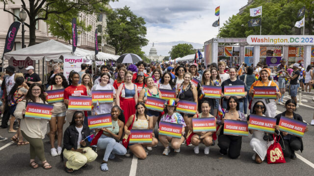 A group of about 20 students pose in two rows, many of them holding signs that say