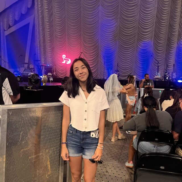 A teenage girl wears a white, button-up casual shirt with short sleeves. She also wears cut-off blue denim shorts. She has shoulder-length dark hair.