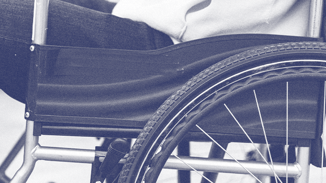 A close-up side profile of a person sitting in a wheelchair; their thighs, torso, and forearm are visible.