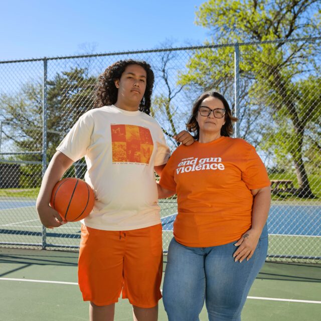 Two people pose for a photo on a community basketball court. One wears the 2025 Wear Orange Future Free From Tee while the other wears the End Gun Violence Retro Tee.