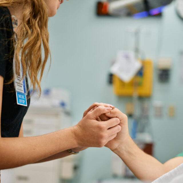 A violence prevention professional holds the hand of a patient in a medical setting, demonstrating the interaction between patients and service providers in a hospital-based violence intervention program at MUSC Health.