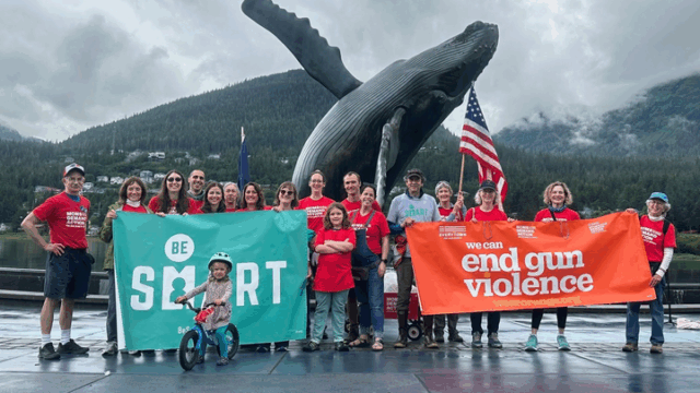 Be SMART volunteers pose for a photo in Alaska. They are wearing red Moms Demand Action shirts and holding two banners, one that reads 