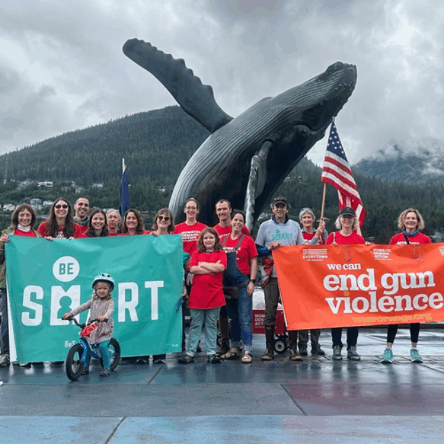 Be SMART volunteers pose for a photo in Alaska. They are wearing red Moms Demand Action shirts and holding two banners, one that reads 